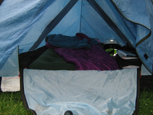 inside a small blue tent filled with airbed, sleepingbag, bags and motorcycle gear